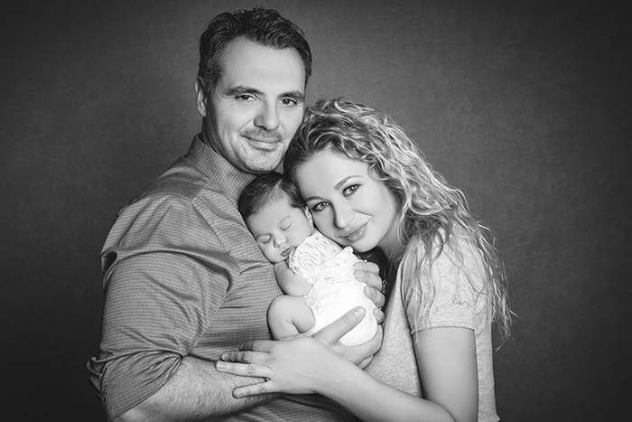 Schwangerschaftsfotografie Babyfotografie Düsseldorf. Eltern kuschelnd mit Baby blicken lächelnd und glücklich in die Kamera. 